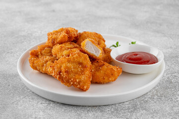Crispy chicken nuggets with ketchup on a white plate on a gray concrete background.