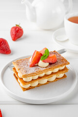 French dessert millefeuille with vanilla cream and fresh strawberries on a white plate on a white...