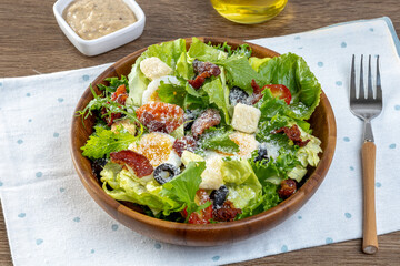 Salad with Fried Bacon, romaine lettuce, tomatoes and sauce known as Caesar salad served on plate, wooden table background