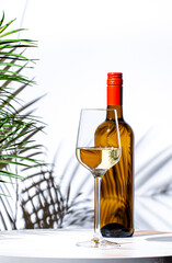 Non-alcoholic, alcohol free, white wine sauvignon blanc in glass with bottle. White background, palm leaves shadows, hard light