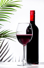 Non-alcoholic, alcohol free, red wine tempranillo in glass with bottle. White background, palm leaves shadows, hard light