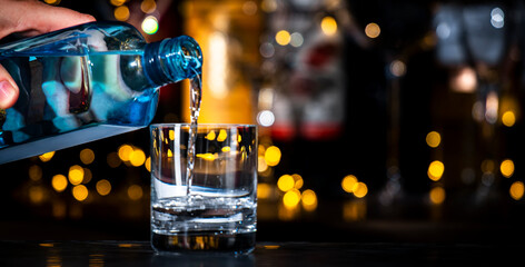 Dry gin pours in glass, strong drinks bottles on black bar counter background with lights