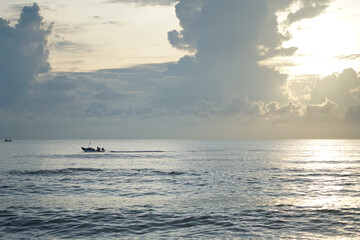 Silhouette of fisherman driving the long-tail boat in the calm sea with sunrise in background