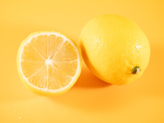 A bright yellow lemon, whole and halved, set against a vibrant orange background