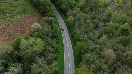Aerial view of Glan Gwan, Caernarfon, capturing a car driving off into the woodland road. This stunning bird's-eye perspective showcases the lush green countryside and charming caravan park.