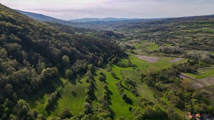 Fototapeta premium Aerial drone view of the stunning green mountains and meadows in Sokobanja, Serbia. The vast natural landscape stretches under the clear blue sky, showcasing the beauty of the region.