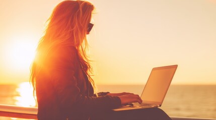 Woman using laptop at sunset by the ocean shore with sunlight glow