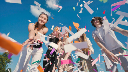 Group of cheerful high school students throwing colorful confetti in the air, celebrating graduation or end of school year