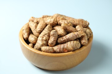 Tumeric rhizomes in bowl on light blue background, closeup