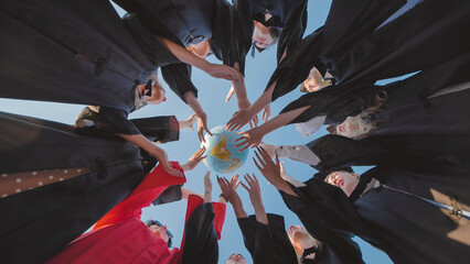 Graduates in academic gowns preparing to seize global opportunities after their graduation ceremony by touching a globe