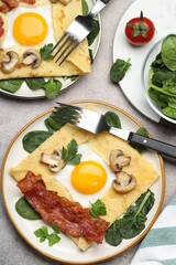 Delicious crepes with eggs, bacon and mushrooms served on grey table, flat lay. Breton galette