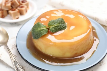 Delicious pudding with caramel sauce and mint on white table, closeup