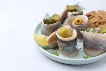 Delicious herring rolls with olives, pickles and dill on light table, closeup. Space for text