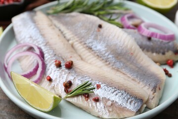 Marinated herring fillets with onion rings, rosemary, lime and peppercorns on table, closeup