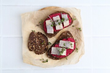 Tasty sandwiches with herring and horseradish sauce on white tiled table, top view
