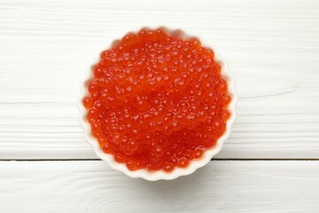 Tasty red caviar in bowl on white wooden table, top view