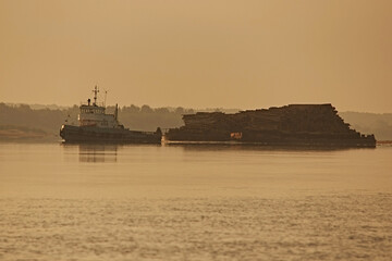 Obraz premium Tugboat and cargo barge carrying timber along river at sunset, close up