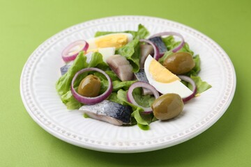 Delicious salad with herring, egg and vegetables on green background, closeup