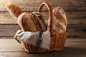 Different loaves of fresh bread in wicker basket on wooden table