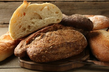Different loaves of fresh bread and knife on wooden table, closeup