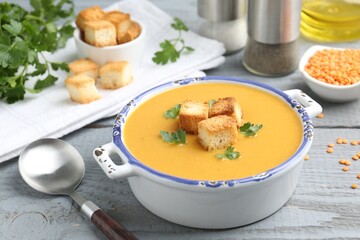 Delicious lentil cream soup served with croutons on grey wooden table, closeup