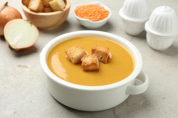 Delicious lentil cream soup served with croutons on light grey table, closeup