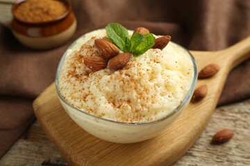 Delicious rice pudding with cinnamon, almonds and mint on wooden table, closeup