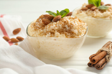 Delicious rice pudding with cinnamon, almonds and mint on white wooden table, closeup