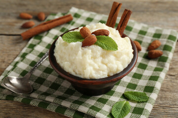 Delicious rice pudding with almonds, mint and cinnamon sticks served on wooden table, closeup