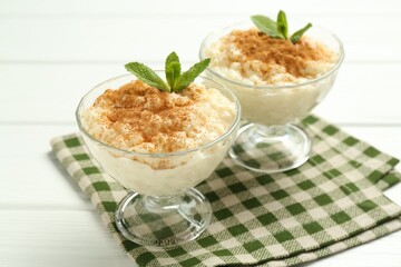 Delicious rice pudding with cinnamon and mint in glass dessert bowls on white wooden table, closeup