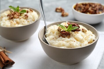 Delicious rice pudding with walnuts, mint and cinnamon on table, closeup