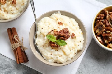 Delicious rice pudding with walnuts, mint and cinnamon on grey table, flat lay