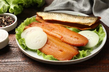 Delicious smoked herring fillets with onions and lettuce on wooden table, closeup