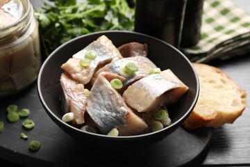 Pieces of delicious herring with green onions on black wooden table, closeup