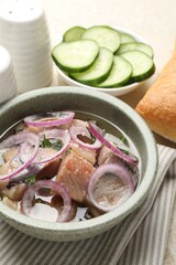 Pieces of delicious herring with onions, cucumber slices and bread on light table, closeup