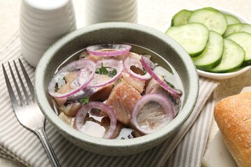 Pieces of delicious herring with onions, cucumber slices and bread on light table, closeup
