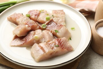 Pieces of delicious herring with green onions on light table, closeup