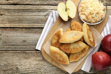 Delicious fried pyrizhky (stuffed pies) and apples on wooden table, flat lay. Space for text