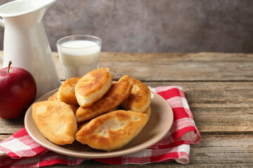 Delicious fried pyrizhky (stuffed pies), milk and apples on wooden table, closeup. Space for text