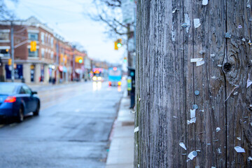 Wooden utility pole with staples from posted handbills right of frame out of focus street scene in background room for text