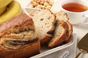 Cut banana bread with nuts, server and tea on table, closeup