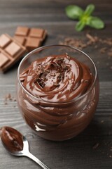 Delicious chocolate pudding in glass and spoon on wooden table, closeup