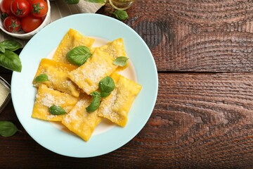 Delicious ravioli with cheese and basil served on wooden table, flat lay. Space for text