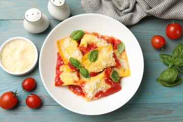 Delicious ravioli with tomato sauce, parmesan cheese and basil on blue wooden table, flat lay