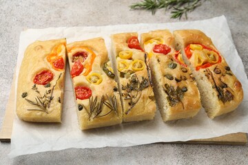 Cut delicious focaccia with flowers made of vegetables on grey table, closeup
