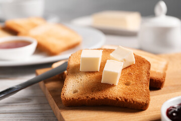 Slices of tasty toasted bread with butter on light wooden table against grey background, closeup
