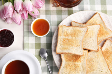 Tasty crispy toasted bread slices, tea and jam on table, flat lay