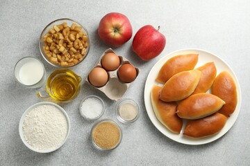 Tasty baked patties and ingredients on light grey table, flat lay