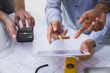 Engineers and architects pointing at digital tablet screens. Two Construction Engineers or Architects discussing at work with digital tablet, laptop and blueprint on construction site.