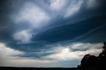 Obraz premium Layered Thunderstorm Clouds Looming Over Forest Landscape